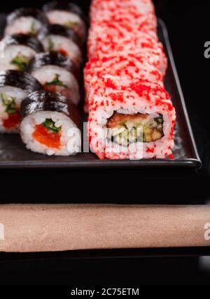 Sushi-Set aus Uramaki und Maki mit rotem Kaviar, Lachs und Gurke. Serviert auf einem schwarzen Teller. Stockfoto