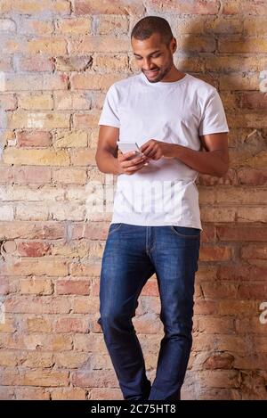 Ein hübscher junger Mann mit seinem Smartphone in ein weißes T-Shirt und eine blaue Jeans. Stockfoto