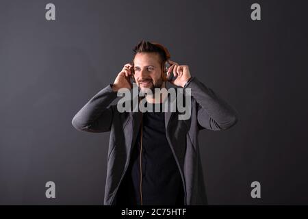 Ein lächelndes hübscher junger Mann in einem grauen kapuzenpullover Musik hören vor einem dunklen Hintergrund grau in einem Studio. Stockfoto