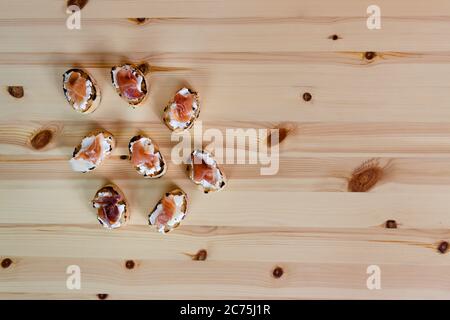 Toast mit Frischkäse und Prosciutto. Draufsicht auf Fingerfood, mediterrane Ernährung. Auf Holzhintergrund. Party-Essen, Baguette-Vorspeise Stockfoto