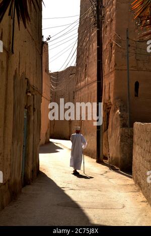 Alter Mann in einem traditionellen omanischen Kleid zu Fuß auf der schmalen Straße in Nizwa, Oman Stockfoto