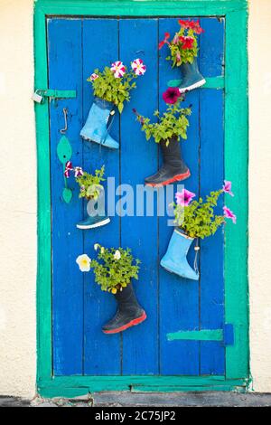 Alte Kinder Gummistiefel mit blühenden Sommerblumen an der Eingangstür eines Hauses Stockfoto