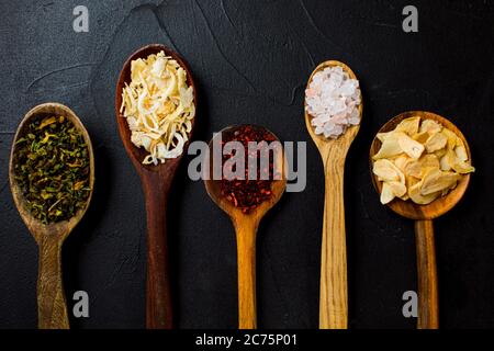 Verschiedene Gewürze in Holzlöffeln auf schwarzem Hintergrund. Stockfoto