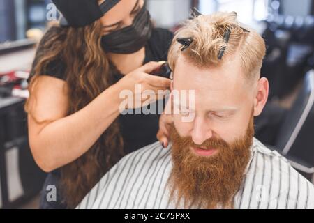 Frisur für Herren in einem Friseurladen. Haarpflege. Barber in Maske Schutz vor Viren. Haarschnitt in Quarantäne. Stockfoto