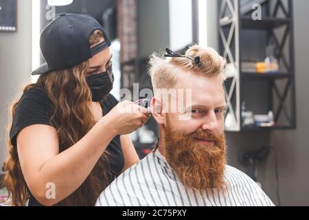 Frisur für Herren in einem Friseurladen. Haarpflege. Frau Friseur in Maske Schutz vor Viren. Haarschnitt in Quarantäne. Stockfoto