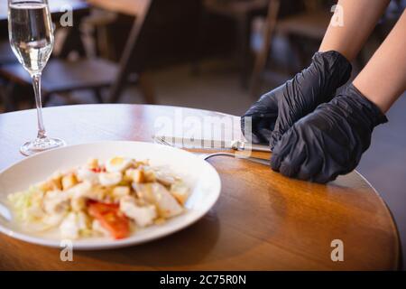 Die Kellnerin arbeitet in einem Restaurant in einer medizinischen Maske, Handschuhe während Coronavirus Pandemie. Stellt eine neue Norm in Service und Sicherheit dar. Bestellung, Bedienung, Betreuung von Kunden, Besuchern. Stockfoto