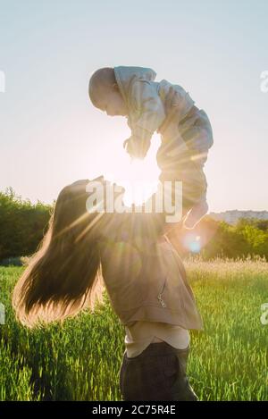 Happy Girl hält ihr Kind in den Armen und wirft ihn an einem sonnigen Tag bei Sonnenuntergang Stockfoto