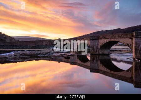 Eine lebendige sunrise Highlights die Bögen des Burnsall Brücke in den Yorkshire Dales, mit den lebendigen Farben in den glatten Flowing River Wharfe wider. Stockfoto