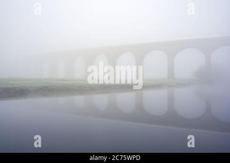 Die markanten Bögen des Arthington Viaduct sind gerade an einem nebligen, frostigen Wintermorgen sichtbar, von den Ufern der River Wharfe aus gesehen. Stockfoto