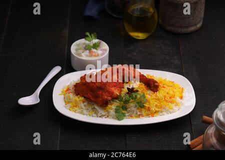 Huhn Biryani , Tandoori Hühnerschenkel mit Basmathi Reis und Raita oder Raitha als Beilage in einem weißen Teller mit schwarzem Hintergrund angeordnet Stockfoto