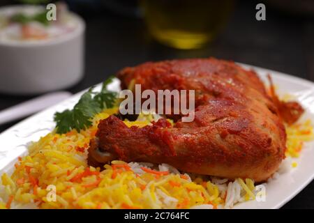 Nahaufnahme des Chicken Biryani , Tandoori Hühnerschenkel mit Basmathi-Reis und Raita oder Raitha als Beilage in einem weißen Teller mit schwarzem Bac angeordnet Stockfoto