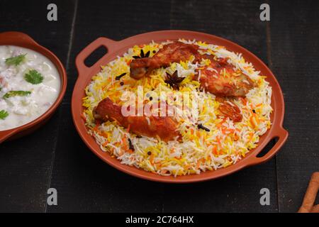 Huhn Biryani , Tandoori Huhn mit Basmathi Reis und Raita als Beilage in einer Terrakotta Steingut mit schwarzem Hintergrund oder Textur angeordnet Stockfoto