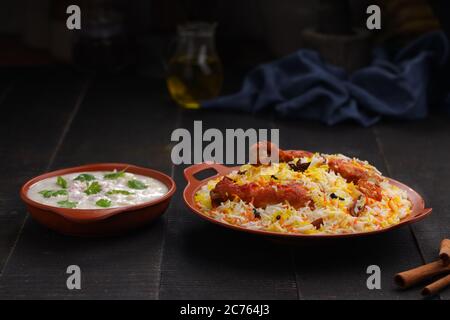 Huhn Biryani , Tandoori Huhn mit Basmathi Reis und Raita als Beilage in einer Terrakotta Steingut mit schwarzem Hintergrund oder Textur angeordnet Stockfoto