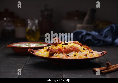 Huhn Biryani , Tandoori Huhn mit Basmathi Reis und Raita als Beilage in einer Terrakotta Steingut mit schwarzem Hintergrund oder Textur angeordnet Stockfoto