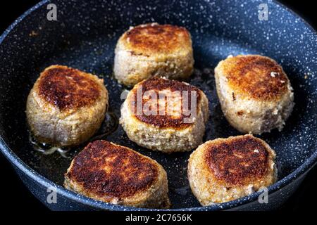 Panierte Hähnchenschnitzel, in einer schwarzen Keramikpfanne mit Pflanzenöl erhitzt. Der Prozess des Bratens von Steaks. Traditionelle Küche. Stockfoto