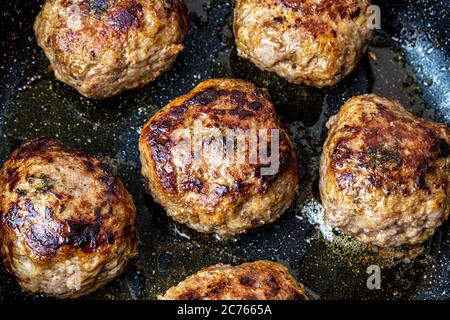 Rinderschnitzel, in einer schwarzen Keramikpfanne mit Pflanzenöl erhitzt. Der Prozess des Bratens von Steaks. Traditionelle Küche. Stockfoto