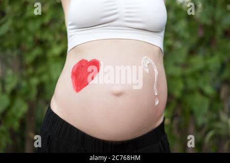 Rotes Herz und Fragezeichen auf einem schwangeren weiblichen Bauch gezeichnet. Schwangeres Konzept. Nahaufnahme Stockfoto