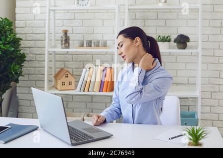 Schmerzen im Nacken. Büroarbeit. Überarbeiteter junger Mann, der an Müdigkeit oder Nackenschmerzen am Arbeitsplatz leidet. Stockfoto