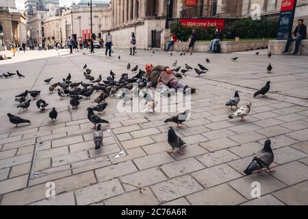 London / UK - 07/11/2020: Der ältere Mann bekam seinen Kopf mit roter Farbe bedeckt und lag auf dem Trafalgar Square neben den Dutzenden Tauben Stockfoto