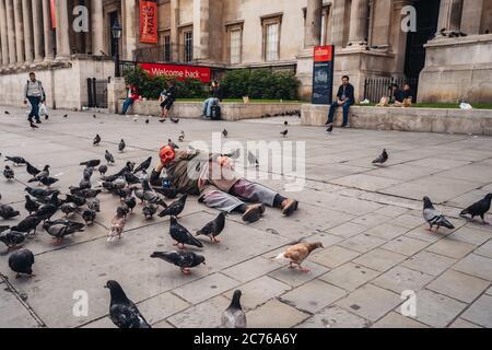 London / UK - 07/11/2020: Der ältere Mann bekam seinen Kopf mit roter Farbe bedeckt und lag auf dem Trafalgar Square neben den Dutzenden Tauben Stockfoto