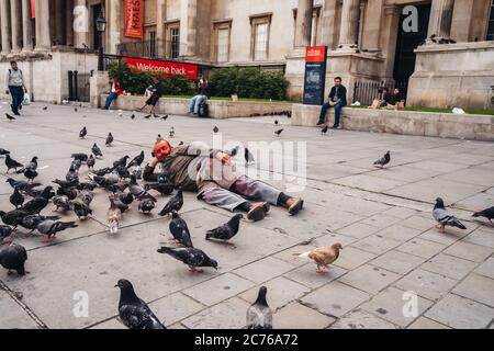 London / UK - 07/11/2020: Der ältere Mann bekam seinen Kopf mit roter Farbe bedeckt und lag auf dem Trafalgar Square neben den Dutzenden Tauben Stockfoto