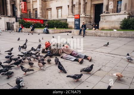 London / UK - 07/11/2020: Der ältere Mann bekam seinen Kopf mit roter Farbe bedeckt und lag auf dem Trafalgar Square neben den Dutzenden Tauben Stockfoto