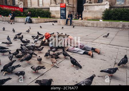 London / UK - 07/11/2020: Der ältere Mann bekam seinen Kopf mit roter Farbe bedeckt und lag auf dem Trafalgar Square neben den Dutzenden Tauben Stockfoto