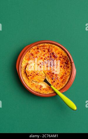 Hausgemachte Crème brûlée in einem Tonblech, auf grünem Hintergrund. Crema Catalana oder Cambridge Brandcreme, ein Pudding Dessert mit Karamellkruste. Stockfoto