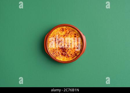 Schale Crème brûlée mit Karamellkruste, in einem Tonblech, auf grünem Hintergrund. Blick von oben auf hausgemachte gebrannte Sahne. Französischer Pudding Dessert. Karamellcreme Stockfoto