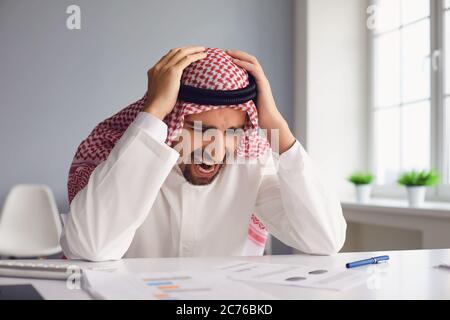 Der Araber hält seinen Kopf mit den Händen, während er an einem Tisch im Büro sitzt. Stockfoto