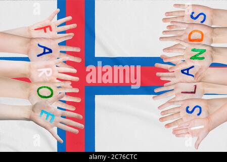 Inschrift Färöer Inseln auf den Kinderhände vor dem Hintergrund einer winkenden Flagge der Färöer Inseln Stockfoto