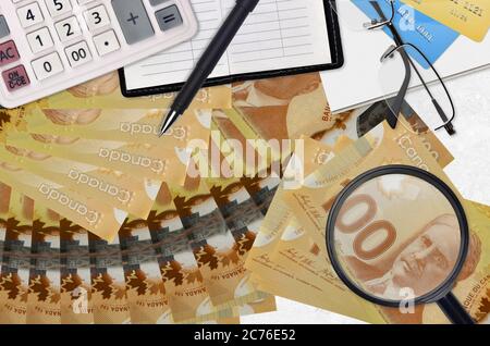 100 kanadische Dollar Rechnungen und Rechner mit Brille und Stift. Tax Payment Saison Konzept oder Investment-Lösungen. Suche nach einem Job mit hohem Gehalt e Stockfoto