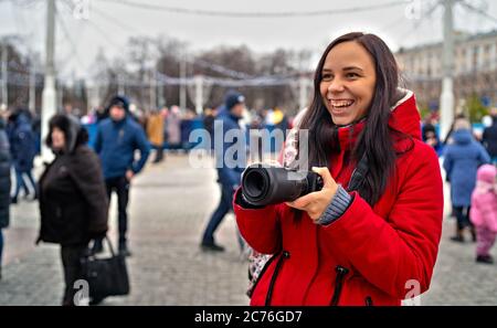 Junge Frau in roter Jacke fotografieren auf einem Spaziergang. Erwachsene Dame hält die Kamera und lacht weit. Nahaufnahme. Stockfoto
