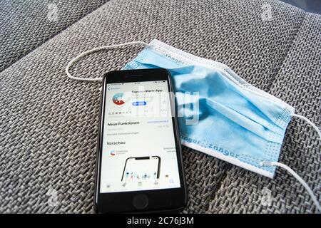 Corona Warn App der Bundesregierung im Apple App Store auf einem Smartphone, das auf einer Schutzmaske liegt. Stockfoto