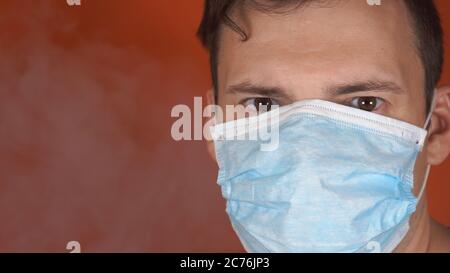 Ein Mann mit einer medizinischen Maske auf seinem Gesicht auf einem orangen Hintergrund. Die Epidemie Des Coronavirus. Stockfoto