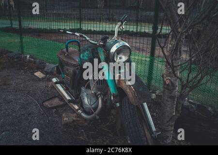 Altes rostiges Motorrad in der Nähe von Zaun auf dem Boden. Nahaufnahme von verlassenen defekten Motorrad. Stockfoto