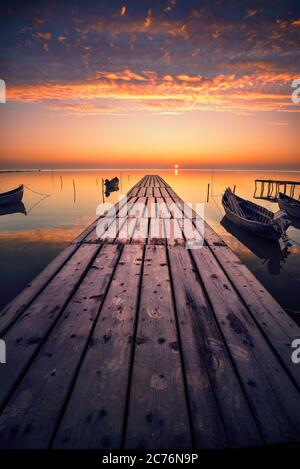 Schöner Sonnenaufgang oder Sonnenuntergang auf dem See mit Fischerbooten und Ponton Stockfoto