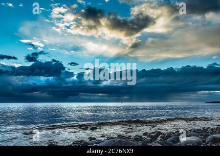 Das Meer nach einem Sturm über der schwedischen Ostsee bei Sonnenuntergang, wo die Sonnenstrahlen zwischen den Wolken aufleuchten und der Himmel wieder blau wird Stockfoto