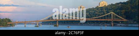Blick auf die Parkovy Fußgängerbrücke über den Dnjepr Fluss, auf der ruhende Menschen spazieren. Stockfoto