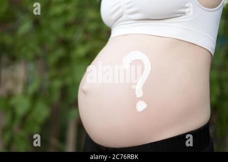 Fragezeichen auf einem schwangeren weiblichen Bauch gezeichnet. Schwangeres Konzept. Nahaufnahme Stockfoto