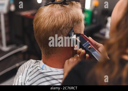 Weibliche Barbier in Maske schneidet einen Mann Haare mit Haarschneider. Frisur während der sozialen Distanzierung Stockfoto