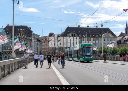 Basel, BL / Schweiz - 8. Juli 2020: Passanten überqueren den Rhein nach Klein Basel mit der Basler Straßenbahn vorbei Stockfoto