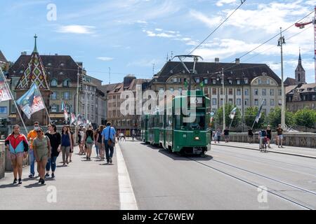 Basel, BL / Schweiz - 8. Juli 2020: Passanten überqueren den Rhein nach Klein Basel mit der Basler Straßenbahn vorbei Stockfoto