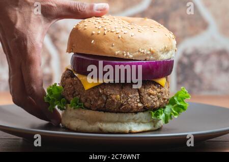 Frauenhände nehmen einen vegetarischen Burger mit Bohnen und Linsen Stockfoto