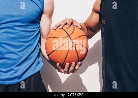 Zwei Basketballspieler verschiedener Rassen halten einen Ball zusammen Stockfoto