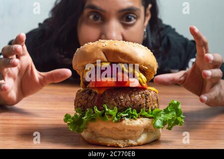 Hübsches mexikanisches Mädchen starrte in Überraschung und packte an großen vegetarischen Burger aus Bohnen und Linsen Stockfoto