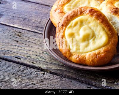 Öffnen Sie die Brötchen mit dem Hüttenkäse (watruschka)liegend in der Tonplatte auf dem hölzernen Tisch. Сlose nach oben.Rustikale Fotografie. Stockfoto