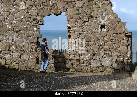 Mädchen mit Schal, der Mund und Nase bedeckt, die durch die Ruinen von Dunluce Castle in der Nähe von Portrush, Grafschaft Antrim, Nordirland, wandern Stockfoto