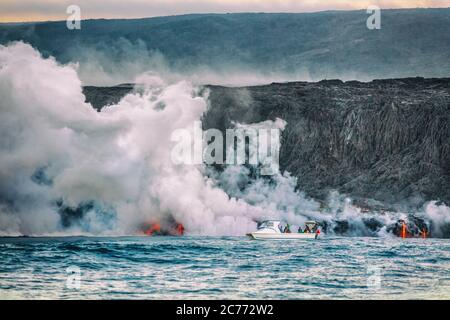 Bootstour zum Vulkanausbruch auf Hawaii. Touristen auf der Bootsfahrt beobachten die Lava, die mit giftigen Dämpfen ins Wasser gelangt. Gefährlicher Ausflug Stockfoto