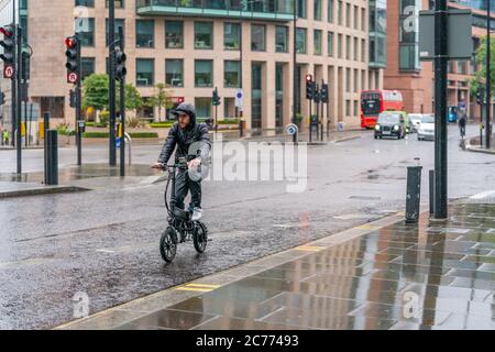 LONDON, ENGLAND - 10. JUNI 2020: Junger Radler, der an einem niesigen Tag mit einem kleinen Brompton-Fahrrad in Holborn, London, während des C im Regen verfing Stockfoto